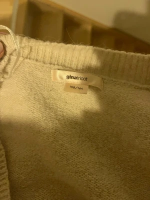 Beige omlottkofta från Gina Tricot - Mysig beige omlottkofta från Gina Tricot med knyt i sidan. Tröjan är stickad och har långa ärmar samt bred ribbad kant nedtill och vid ärmsluten. Perfekt för lager på lager under höst och vinter.
