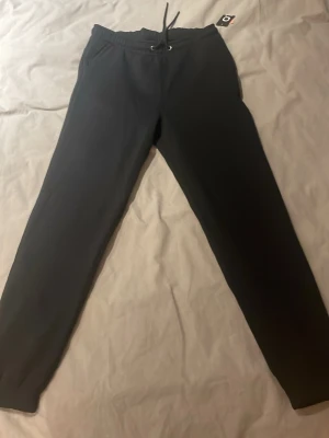 Svarta mjukisbyxor med snörning - Säljer ett par svarta mjukisbyxor med elastisk midja och snörning framtill. Byxorna har en enkel och clean design, raka ben och är tillverkade i mjukt material som känns skönt mot huden. Perfekta för chill dagar eller när du vill vara bekväm.