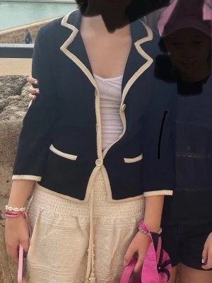 Svart kofta med vita detaljer Filippa K - Stilren svart kofta från Filippa K med kontrasterande vita kanter och knappar. Klassisk krage, två fickor framtill och trekvartsärm. Perfekt för en snygg och uppklädd look. Materialet känns mjukt och bekvämt.