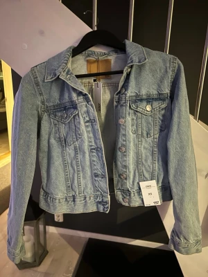 Ljusblå jeansjacka  - Säljer en snygg ljusblå jeansjacka. Jackan har klassisk krage, knappar framtill och två bröstfickor med lock. Perfekt att slänga över en hoodie eller t-shirt för en chill look.