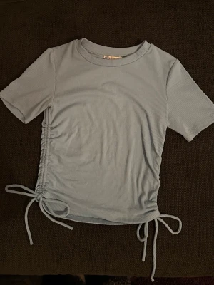 Ljusblå ribbad topp från Zara - Säljer en ljusblå ribbad topp från Zara i storlek S. Toppen har korta ärmar, rund halsringning och snygga snörningsdetaljer i sidorna. Använd men i mycket fint skick 