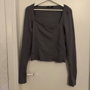 Grå ribbad långärmad topp Gina Tricot - Säljer en stilren grå ribbad topp från Gina Tricot med lång ärm och fyrkantig halsringning med slits vid armarna . Toppen har en slim passform . Perfekt att styla med jeans eller kjol för en cool look.