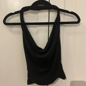 Svart halterneck topp från Bershka - Säljer en svart halterneck topp från Bershka i slät polyester. Toppen har en snygg draperad framsida och öppen rygg. Aldrig använd.