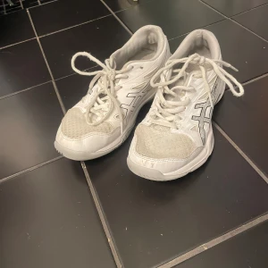 Vita Asics sneakers strl 37 - Säljer ett par vita Asics sneakers i storlek 37. Skorna har klassisk sportig design med mesh och syntetdetaljer, snörning och rund tå. Perfekta för dig som gillar en clean och enkel look till vardags eller träning.Kan ge skavsår i ena skon men har inte hänt.
