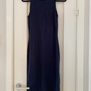 Marinblå långklänning Emporio Armani - Snygg marinblå långklänning från Emporio Armani i storlek 40. Klänningen är ärmlös med rund hals och har en diskret struktur i tyget som ger en exklusiv känsla. Passformen är normal och materialet känns mjukt och lyxigt. Perfekt för dig som gillar stilrena och klassiska plagg.Storleken är 40 men den är liten i storleken och är mer en europeisk strl 38 dubbelkolla måtten nedan.   Mått  Över bröstet: ca 39 cm  Över höften: ca 42 cm  Längd från axeln och ner: ca 102 cm  