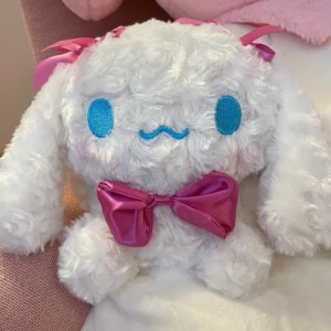 Cinnamoroll Plush - Supermjuk Cinnamoroll-mjukisdjur från Sanrio, med blå broderade ögon, rosa rosett och rosetter på öronen. Mycket fint skick, inga synliga defekter eller slitage. Perfekt för samlare eller som present till någon som älskar kawaii och Sanrio-karaktärer. 20 cm x 22 cm