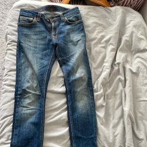 Blå jeans från Nudie Jeans, storlek 29/32 - Snygga blå jeans från Nudie Jeans i storlek 29/32. Modellen har klassisk femficksdesign, orangea sömmar och en straight passform med något tapered ben. Jeansen är tillverkade i slitstarkt bomullsmaterial och har coola slitningar framtill och bakfickor med broderad detalj. Skriv gärna om du har frågor 🤗
