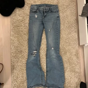 Blå bootcut jeans med slitningar - Säljer ett par ljusblå bootcut jeans med snygga slitningar och trasiga detaljer på benen. Jeansen har klassisk femficksdesign, låg midja och är tillverkade i mjukt denimtyg. Perfekta för dig som gillar en avslappnad och trendig look. Säljer pga att de är lite korta på mig och börjar blir för små! Tveka inte att fråga om du undrar något!💕💕