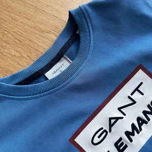 Blå GANT Le Mans sweatshirt - Säljer en blå sweatshirt från GANT med stort Le Mans 24H-tryck på bröstet. Tröjan har rund hals, ribbade muddar och är tillverkad i mjuk bomull. Perfekt för dig som gillar sportig och stilren look.