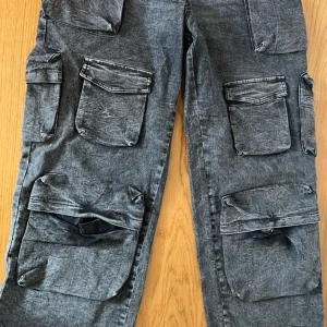 Grå cargopants med stora fickor - Säljer ett par grå cargopants med tvättad look och flera stora fickor framtill och på sidorna. Byxorna har en loose passform och är perfekta för en avslappnad streetstil. Materialet känns som bomull med superstretch och de har en cool, sliten finish.
