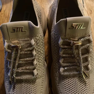 Beige glittriga sneakers Steve Madden - Snygga chunky sneakers från Steve Madden i beige stickat material med glittriga detaljer och snörning. Skorna har en tjock sula och coola metallicdetaljer på snörena samt logga framtill. Perfekta för dig som vill sticka ut med stilrena men ändå blingiga skor. Knappt använda