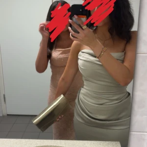 Ljusgrön långklänning i satin - Supersnygg långklänning i champagnefärgad satin med draperad överdel och figurnära passform. Klänningen är axelbandslös och har en elegant, svepande siluett som ger en lyxig känsla. Perfekt för dig som vill sticka ut med en stilren och trendig look.