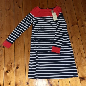 Randig klänning Holly & Whyte Lindex - Mysig höstklänning. Superfin randig klänning från Holly & Whyte by Lindex i marinblått, vitt och rött. Klänningen har långa ärmar med röda muddar och guldiga knappar, samt röda detaljer upptill. Tillverkad i mjuk bomull och har en klassisk, avslappnad passform. 