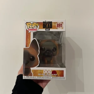 Funko Pop! The Walking Dead Dog #891 - Samlingsfigur Funko Pop! Dog från The Walking Dead, nummer 891. Figuren är i originalförpackning som ser ut att vara i mycket gott skick, perfekt för samlare och fans av serien. Ingen synlig skada eller slitage på boxen.