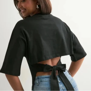 Svart topp med rosett på baksidan - Svart topp med breda korta ärmar och snygg öppen rygg. Toppen har ett stort knytband i midjan som ger en cool detalj och markerar siluetten.