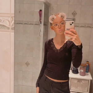 Svart långärmad topp med spets - Säljer en svart långärmad topp med v-ringning och fina spetsdetaljer vid halsringning och ärmslut. Modellen är figurnära och något croppad, perfekt för dig som gillar en stilren men ändå söt look.