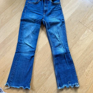 Blå bootcut jeans från Zara - Snygga blå jeans med bootcut passform och rå, fransad kant längst ner på benen. Klassisk femficksmodell och slitningar på framsidan. Jeansen är midwaist. De är tillverkade i jeansmaterial och har en rak, något utsvängd siluett. Storlek 34. Från Zara
