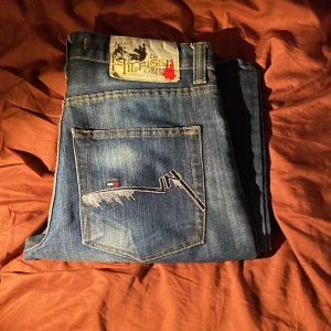 Tommy Hilfiger blå jeans straight fit - Snygga blå jeans från Tommy Hilfiger med cool broderad bakficka och läderpatch med logga. Jeansen har en rak/relaxed passform och klassisk femficksdesign. Materialet är slitstarkt denim och färgen har snygga ljusa tvättade partier för en trendig look. Storleken w31 l34 och pris går att diskutera!