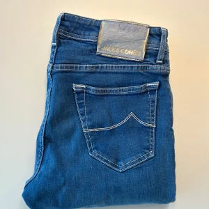 Blå jeans från Jacob Cohen - Snygga blå jeans från Jacob Cohen med klassisk femficksdesign och kontrastsömmar. Jeansen har en slim passform och är tillverkade i mjukt denimtyg med stretch för extra komfort. Perfekta för dig som gillar en stilren och modern look nu till hösten🍂🍂