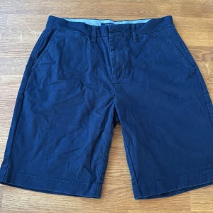 Marinblå shorts Tommy Hilfiger - Snygga marinblå shorts från Tommy Hilfiger med klassisk design och raka ben. De har fickor fram och bak, bälteshällor och stängs med knapp och dragkedja. Materialet är mjuk bomull, perfekt för varma dagar. Diskret Hilfiger-logga på bakfickan. 29 motsvarar S ungefär, lite hårig annars grymt skick