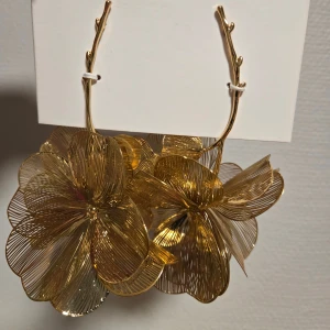 Stora blommiga örhängen i guld - Unika och iögonfallande örhängen i guldmetall med stora, detaljerade blommor. Blommorna har en tunn, trådig design som ger ett lyxigt och trendigt uttryck. Perfekt för dig som vill sticka ut och addera lite extra glamour till din look.