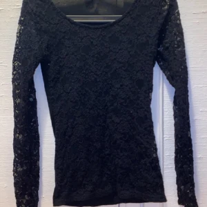 Svart spetsblus med lång ärm - Säljer en svart blus i spets med långärmade ärmar och rund halsringning. Toppens spetsmönster ger en snygg och elegant look, perfekt att styla med jeans eller kjol. Materialet är mjukt och följsamt för en bekväm passform.