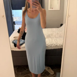 Klänning - Säljer en ljusblå långklänning med smala axelband och figurnära passform. Klänningen är enkel och stilren, perfekt för varma dagar. Materialet känns mjukt och stretchigt, vilket gör den superbekväm att bära.