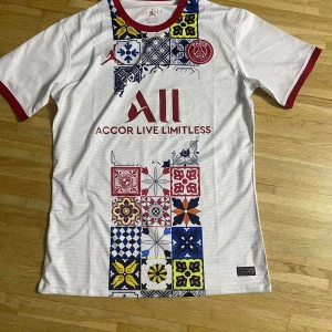 PSG x Jordan vit fotbollströja - Snygg vit PSG fotbollströja från Jordan med röda detaljer vid krage och ärmslut. Framsidan har färgglada grafiska mönster i blått, rött, gult och svart samt klubbmärke och sponsortryck. Tillverkad i lätt och ventilerande material, perfekt för match eller träning.