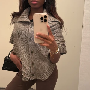 Trekvartsärm poncho/cape med stora knappar - Stickad trekvartsärm poncho/cape med stora knappar framtill. Ponchon har en bred krage och snygga stickade detaljer längs kanterna ❄️🍂🎀