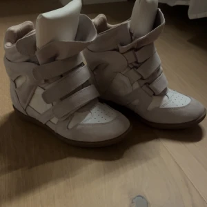 Isabel Marant wedge sneakers beige - Säljer ett par wedge sneakers från Isabel Marant i beige och vitt med platt sula och rund tå. Skorna har flera breda kardborreband och är tillverkade i mocka och skinn. Dem är i strl 38 och oanvända💕
