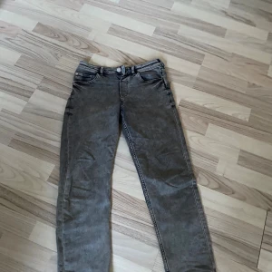 Grå jeansbyxor  - Snygga grå jeansbyxor i rak passform med klassiska fem fickor och knappstängning. Byxorna har en neutral grå färg och är tillverkade i slitstarkt jeanstyg, perfekta för dig som gillar enkel och stilren look.