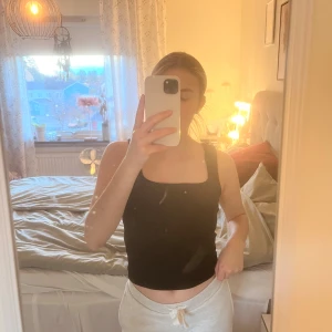 Svart croppad linnetopp - Säljer en svart croppad linnetopp med breda axelband och fyrkantig halsringning. Toppen är ärmlös och har en stilren, enkel design som passar perfekt till jeans eller kjol. Materialet känns mjukt och stretchigt mot huden. Skriv om ni har några frågor ❤️