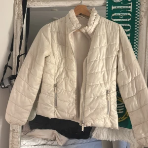 Beige/ off white quiltad pufferjacka från OKAY - Lättvikt jacka. Passar en xxs eller barn 146/152. Off white/ beige pufferjacka från OKAY med quiltad design och hög krage. Jackan har två fickor med dragkedja och en stilren patch på ärmen. Perfekt för kyligare dagar och enkel att matcha med olika outfits.