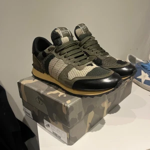 Valentino Rockrunner  - Snygga Valentino Rockrunner sneakers med camouflagemönster i olivgrönt, beige och svart. Skorna har detaljer i mocka och skinn, snörning och en platt sula med nitar på hälen. Perfekt för dig som gillar streetstyle och exklusiva märken.