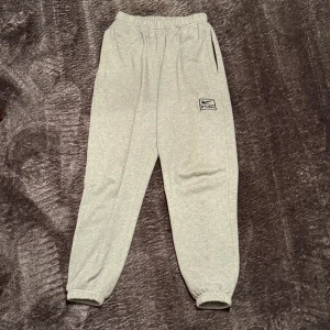 Nike x Stussy sweatpants  - Grå mjukisbyxor från Nike x Stussy med broderad logga på benet. Byxorna har resår i midjan och vid bensluten, samt sidofickor. Tillverkade i mjuk bomullsmix för maximal komfort och avslappnad stil. Storlek L