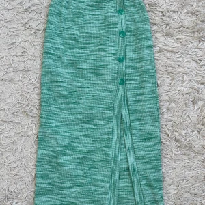 Grön ribbad långkjol  - Snygg grön ribbad långkjol från Gina Tricot i storlek XS. Kjolen har knappar framtill och en liten slits nertill. Melerad grön färg och stretchigt material som sitter skönt. 
