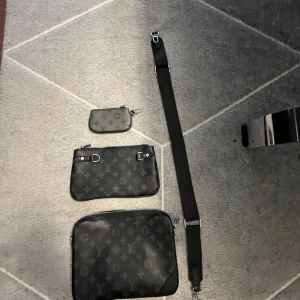  svart axelväska set - Snyggt set med tre svarta väskor från   i klassiskt monogrammönster. Setet inkluderar en axelväska, en mindre handväska och en plånbok, alla med silverfärgade detaljer och dragkedja. Väskorna är tillverkade i skinn och har en justerbar axelrem.