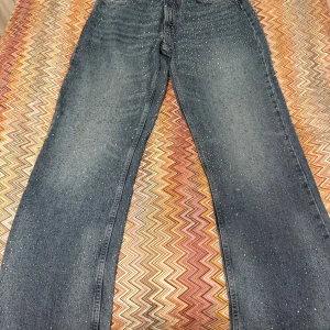 Blå jeans med glitterdetaljer - Säljer ett par blå jeans med raka ben och glittriga paljett-detaljer över hela byxorna. Jeansen har klassisk femficksmodell och normal passform. Perfekta för dig som vill sticka ut lite extra med en cool och unik look.