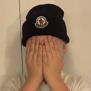 Svart Moncler mössa i ribbstickad ull - Säljer en svart ribbstickad mössa från Moncler med klassisk uppvikt kant och broderad logotyp framtill. Mössan är tillverkad i mjuk ull och har en enkel, stilren design som passar perfekt till kalla dagar. Grisch Laidback 