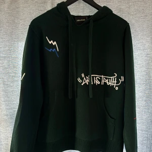 Mörkgrön hoodie Zadig & Voltaire - Säljer en mörkgrön hoodie från Zadig & Voltaire med broderad text 'ART IS TRUTH' och coola grafiska detaljer i vitt och blått. Ny pris 5500kr och tillverkas inte längre 