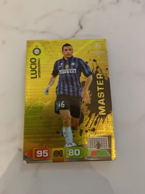 Gul fotbollssamlarkort MASTER Inter - Säljer ett exklusivt fotbollssamlarkort med guldfärgad bakgrund från Panini. Kortet visar en spelare i Inter Milans blåsvarta matchställ och har texten MASTER samt spelarens namn och stats. Perfekt för samlare av fotbollskort!