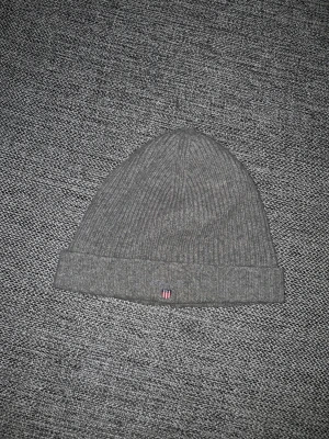 Gant Mössa - Snygg grå ribbstickad mössa från Gant med uppvikt kant och liten broderad logga framtill. Perfekt för kalla dagar och enkel att matcha med olika outfits. Klassisk och stilren design som funkar året runt.