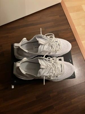Vita Nike React sneakers - Snygga helvita Nike React sneakers med ventilerande meshmaterial och cool snörning. Skorna har en sportig design med rund tå och platt sula, perfekta för dig som gillar stilrena och bekväma sneakers. Oanvända. Köptes för 2000 pris kan diskuteras vid snabb affär.