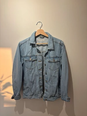 Ljusblå klassisk jeansjacka - Säljer en ljusblå jeansjacka med klassisk passform. Jackan har två bröstfickor med knappar, knappstängning framtill och långa ärmar. Passar xs-m, knappt använd!!