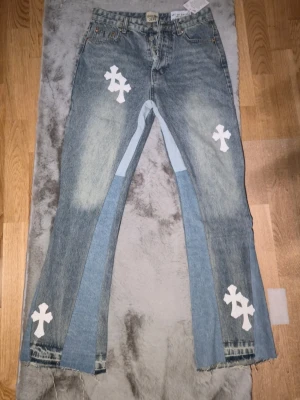 Flared jeans gallery dept - Unika blå jeans från Gallery Dept. med ljusare denim-paneler och råa kanter. Byxorna har vita korsapplikationer på fram- och baksida samt en relaxed, något utsvängd passform. Klassisk femficksmodell med knappgylf och cool vintagekänsla. Pris kan diskuteras vid snabb affär. 