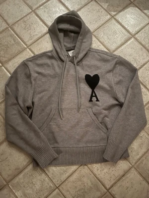 Ami Paris hoodie  - Snygg grå hoodie från Ami Paris med svart hjärta och bokstaven A broderat på bröstet. Hoodien har huva,magficka och ribbade muddar. Perfekt för en chill och trendig look. Storlek S,nästan helt oanvänd! Hör bara av er om ni undrar något!