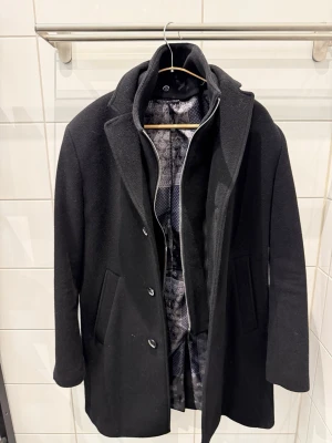 Svart Rock Herr - Svart rock herr  Sparsamt använd och i fint skick Avtagbar väst krage  Storlek: 48 Modern fit  Märke: Stones Material: 70% wool 20% polyamid 10% cashmere