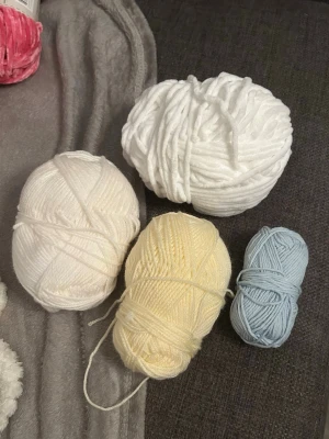 Fyra nystan garn i ljusa färger - Säljer fyra nystan garn i olika färger: ett tjockt vitt, ett ljusgult, ett ljusblått och ett cremevitt. Perfekt för stickning eller virkning av egna projekt. Garnen är mjuka och i olika tjocklekar.