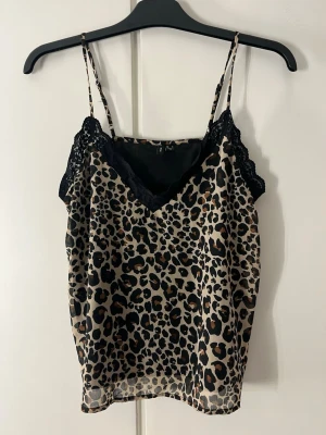 Leopardmönstrad linnetopp med spets - Snygg leopardmönstrad linnetopp med tunna axelband och svart spetsdetalj vid v-ringningen. Perfekt för dig som vill sticka ut och addera lite edge till din outfit. Luftigt material och trendig look.