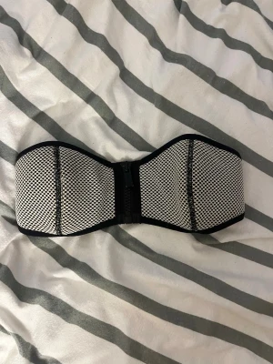 Svartvit bandeau bikiniöverdel TRIANGL - Säljer en snygg bandeau bikiniöverdel i svartvitt meshmönster. Överdelen har dragkedja framtill och breda kanter för extra stöd. Perfekt för dig som vill ha en stilren och sportig look på stranden. Från triangl i storlek S men passar snarare XS🥰